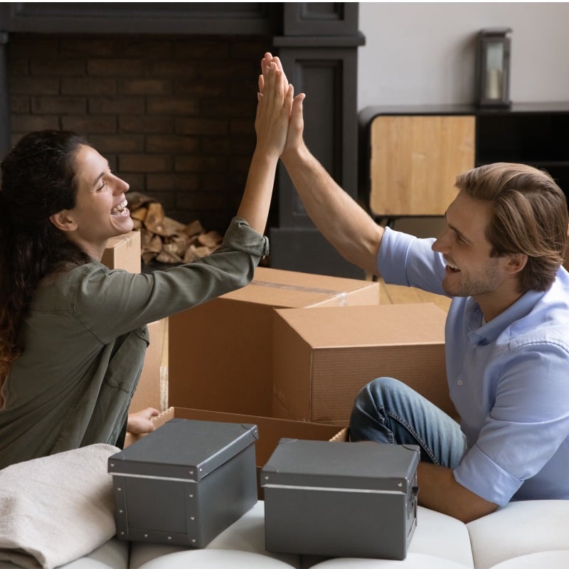man and woman high fiving with moving boxes in the background