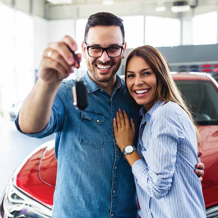 Young couple holding keys in front of red vehicle