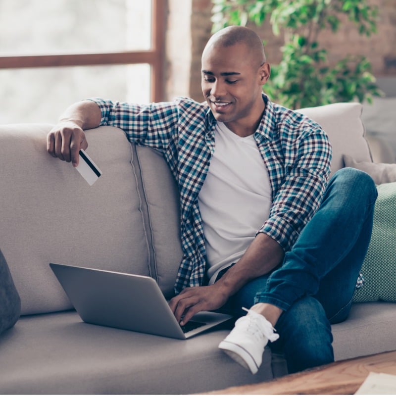 Young Man Holding Debit Card Shopping On Laptop