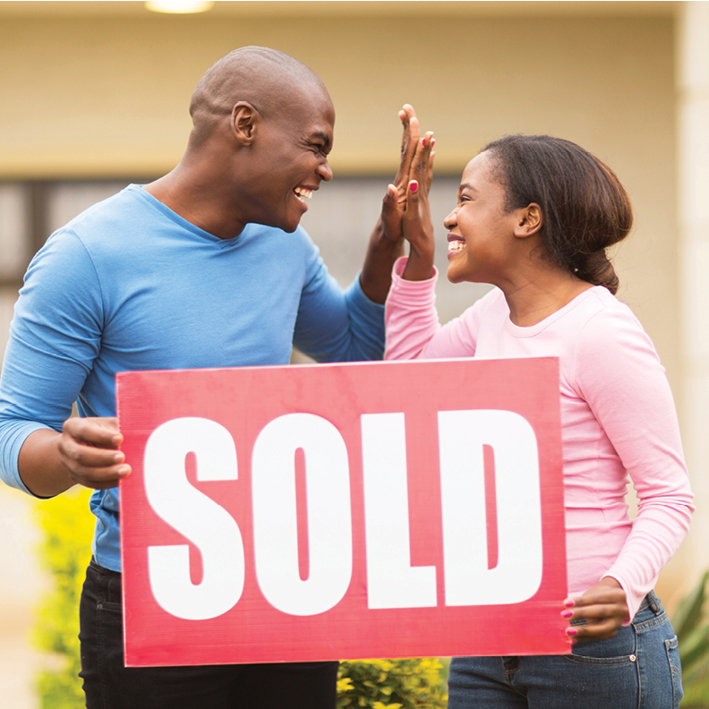 Young_Couple_High_Fiving_Holding_Sold_Sign