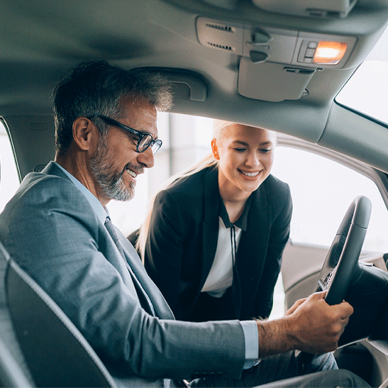 female business banker leaning into car of happy man after refinancing his auto loan