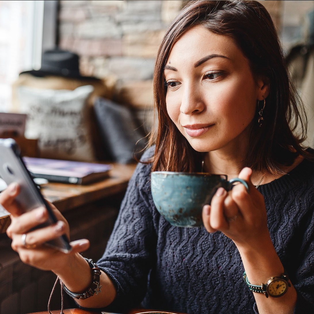 young woman holding coffee mug and looking at her cell phone
