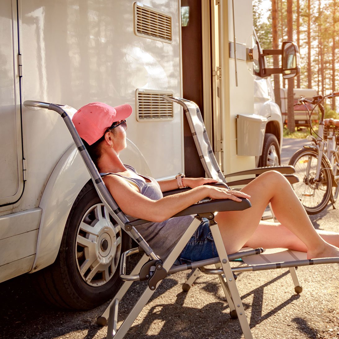 woman in baseball hat and sunglasses sitting on a lawn chair outside an rv
