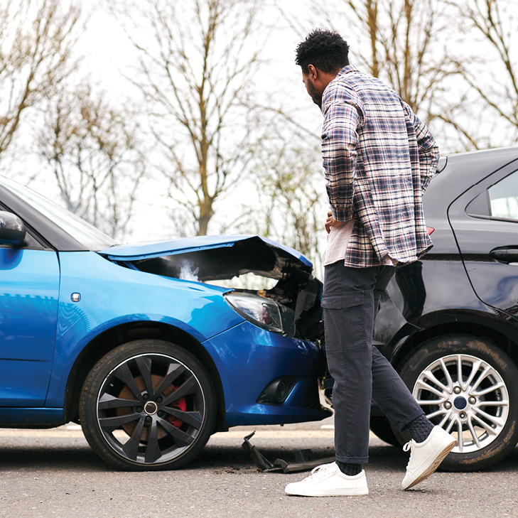 young man looking at his damaged blue car 