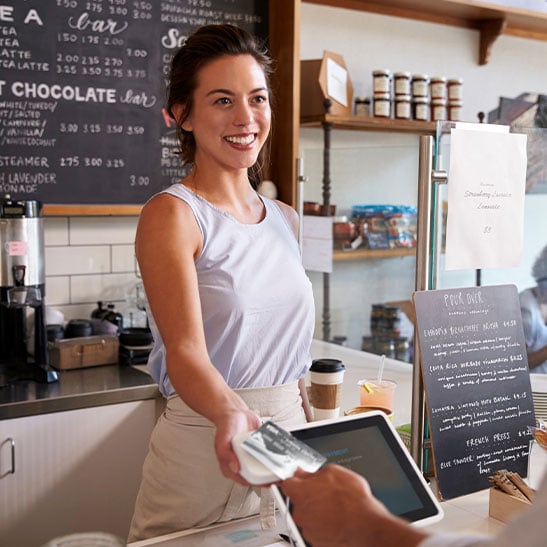 hand holding credit card above credit card machine being held by coffee shop worker