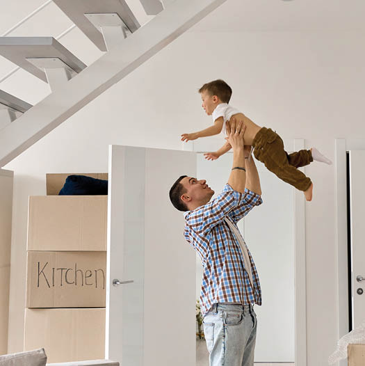 Dad lifting young son in air underneath the stairs of new home purchase