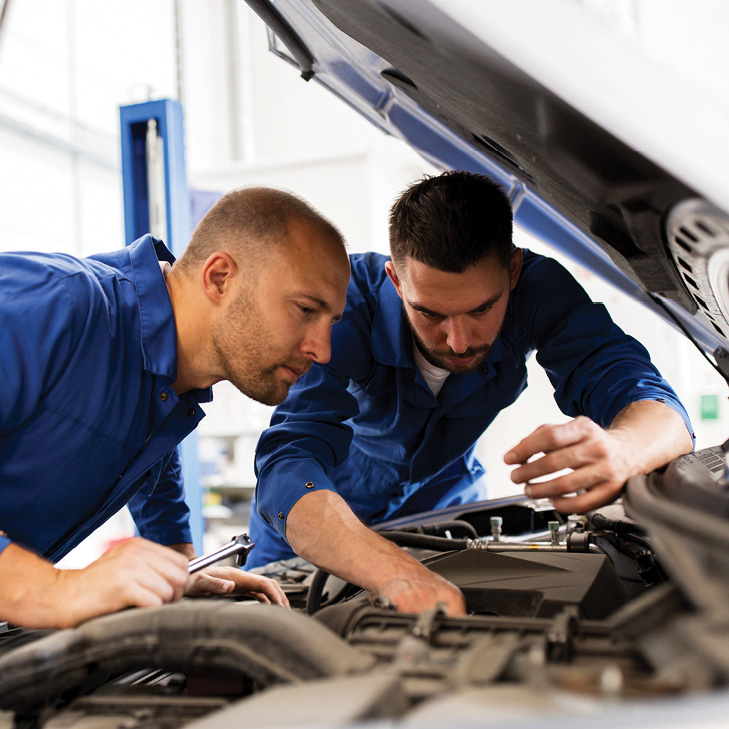 Two mechanics in blue jumpsuits working on car engine