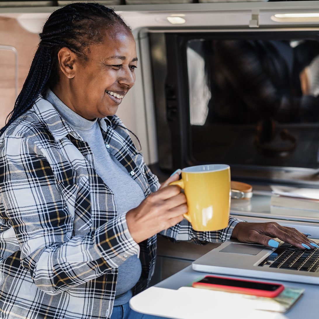 woman smiling with a coffee mug in her hand and typing on a laptop