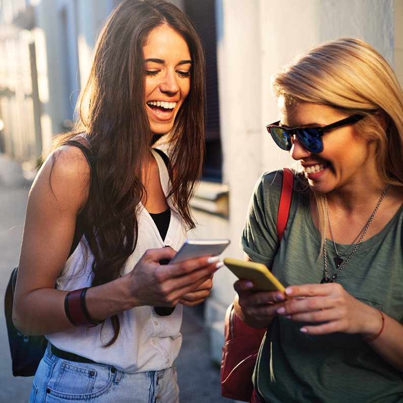 two young ladies smiling and looking at their mobile phones