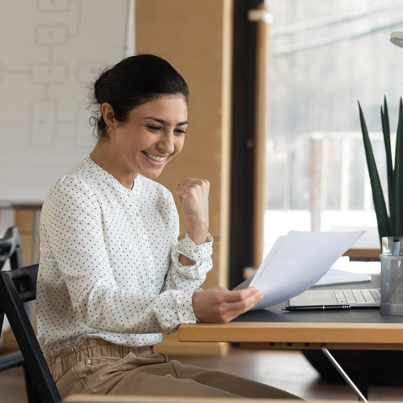 young woman holding personal loan paperwork at a desk very excitingly