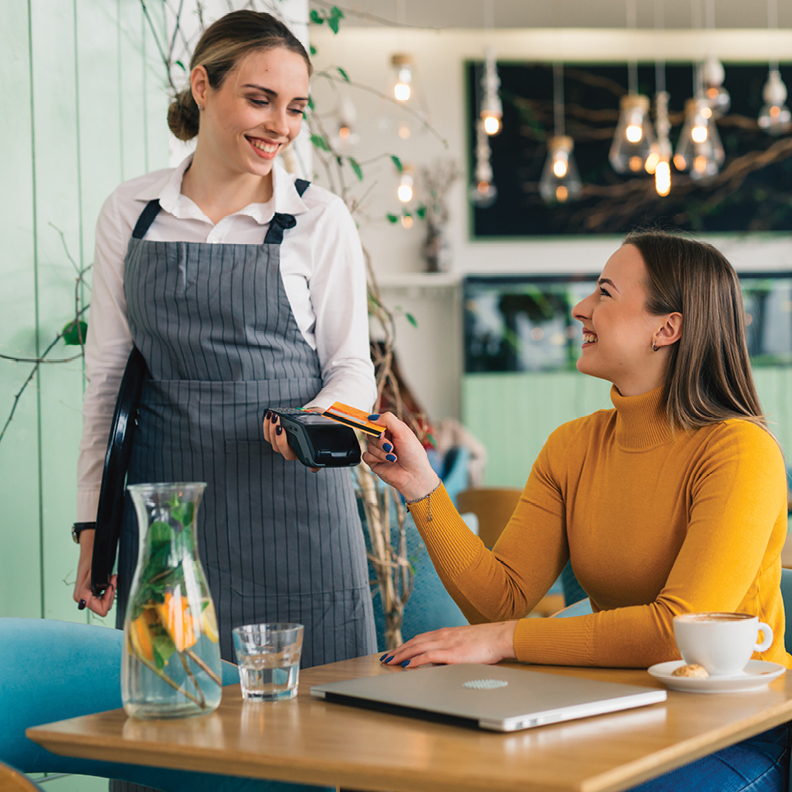 woman sitting at table inserting credit card into credit card machine held by female employee