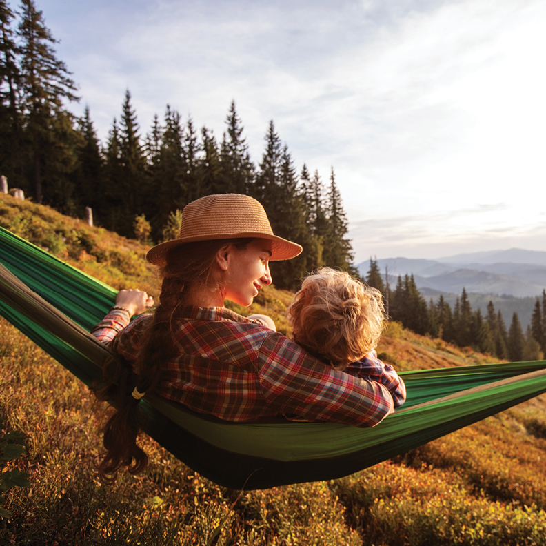 young woman with young child sitting on hammock with a mountain view