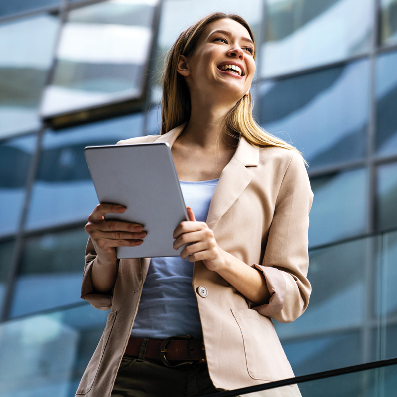 woman in beige blazer smiling while holding a tablet