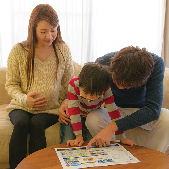 man and pregnant woman sitting with a young boy pointing at learning guide