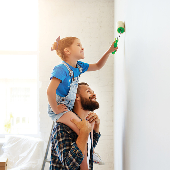 young girl painting a wall while sitting on fathers shoulders