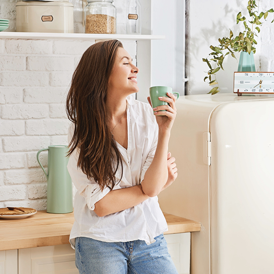 young lady leaning against countertop holding a coffee mug while smiling 