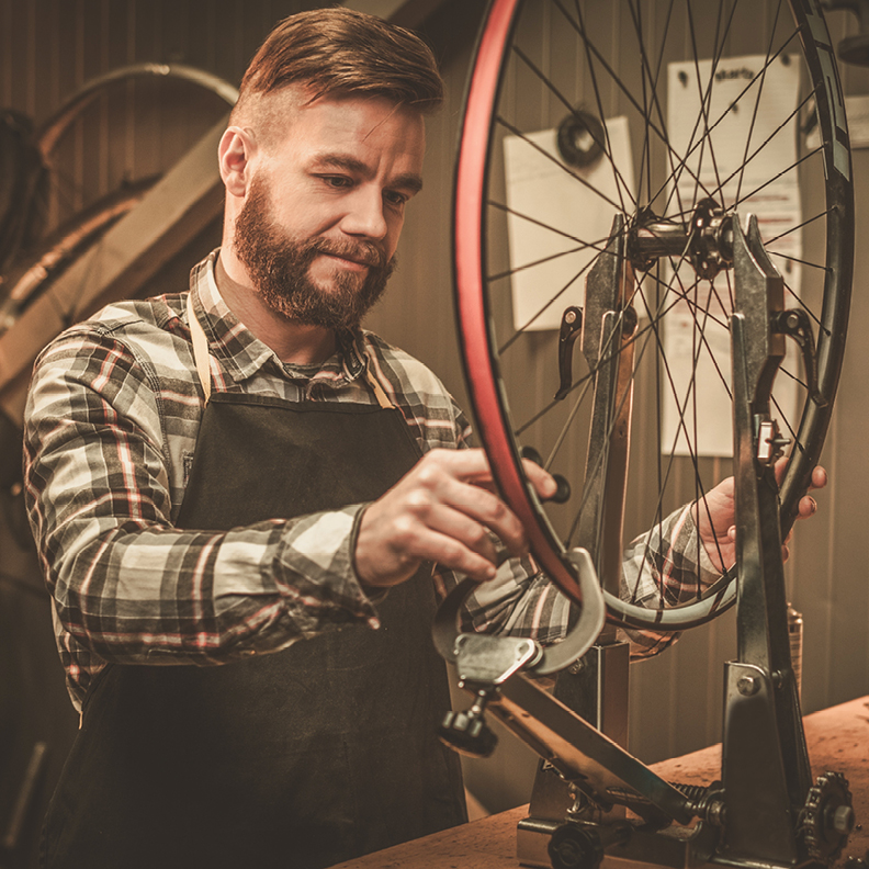 bearded man in apron working on a bicycle wheel 
