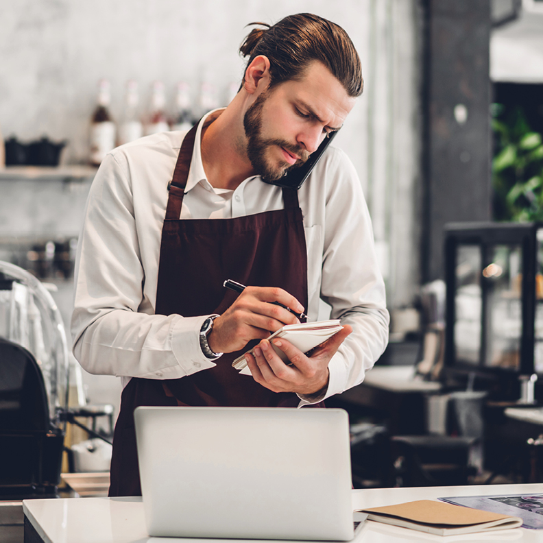 man wearing apron on the phone and writing on a notepad