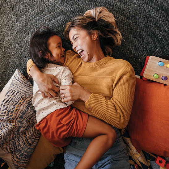 young woman with daughter laying on floor laughing