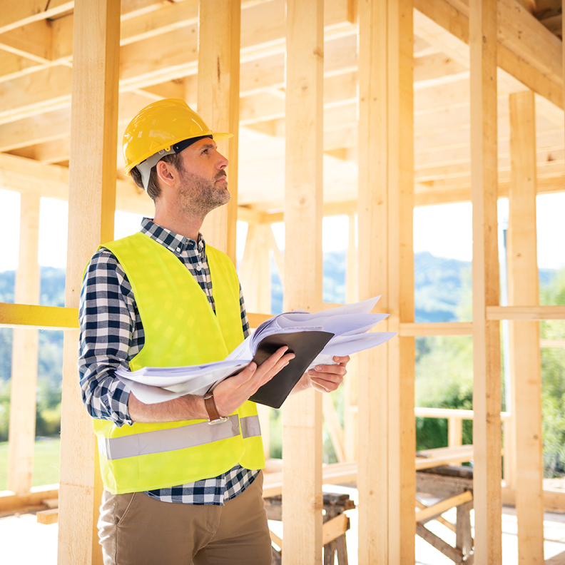 man with hard hat looing up while holding paperwork in a construction site