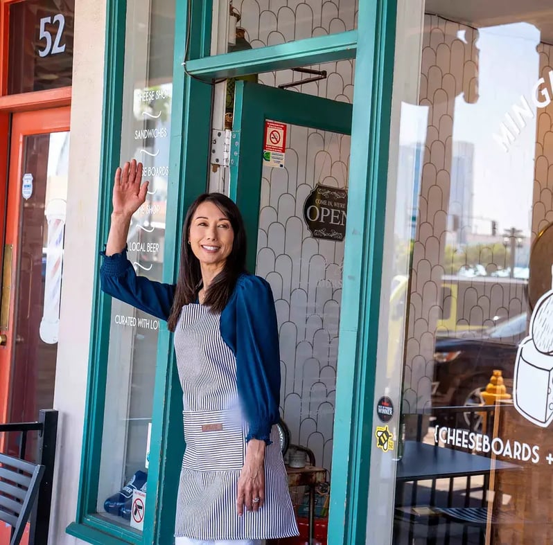 woman-business-owner-waving-outside-her-shop